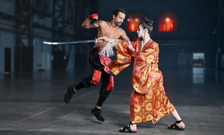A dynamic martial arts cosplay scene featuring a kimono-clad fighter and a tattooed fighter in motion, indoors.