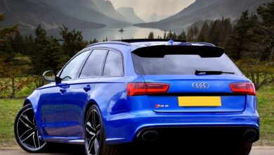 A sleek blue Audi RS 6 wagon parked against a stunning backdrop of Scottish hills and a serene lake.