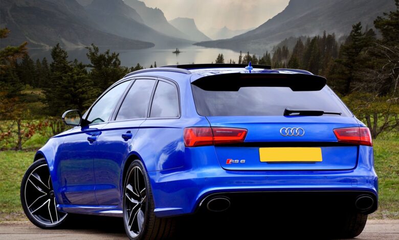 A sleek blue Audi RS 6 wagon parked against a stunning backdrop of Scottish hills and a serene lake.