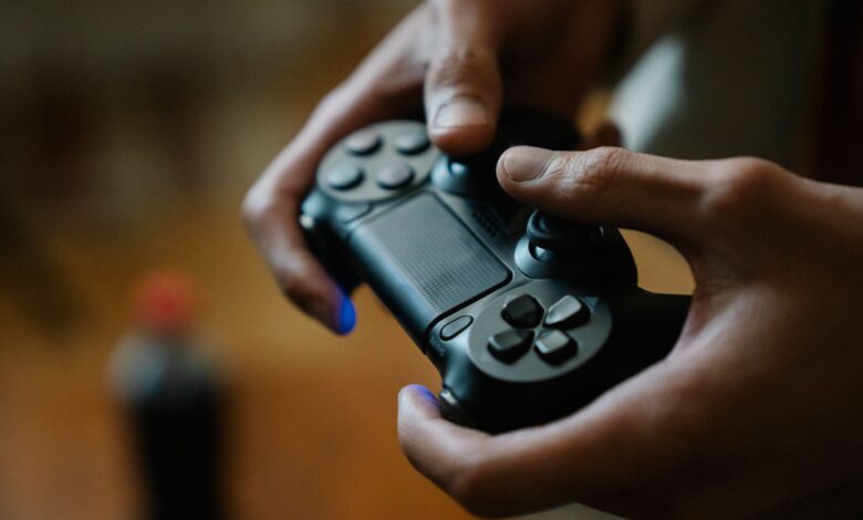 Crop anonymous male pressing buttons on console controller while playing video game in house on blurred background