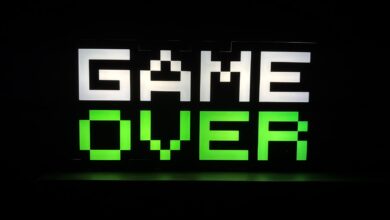 Illuminated 'Game Over' sign in pixel art style with neon green and white colors on a dark background.