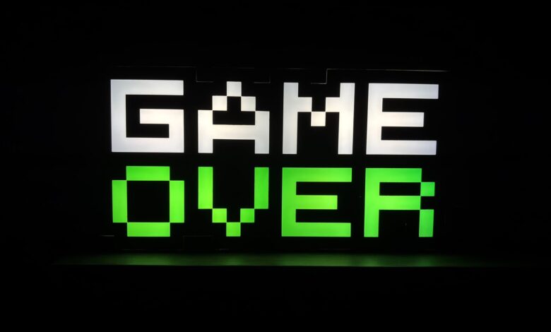 Illuminated 'Game Over' sign in pixel art style with neon green and white colors on a dark background.