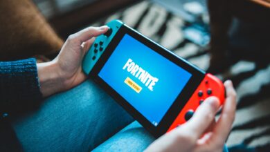 Close-up of hands holding a Nintendo Switch with Fortnite game screen indoors.