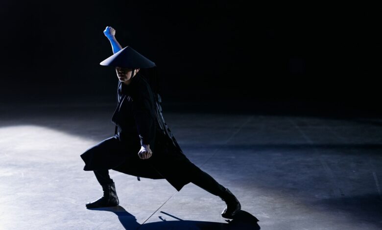 A skilled cosplayer strikes a dramatic pose as a game character in a dark studio setting.