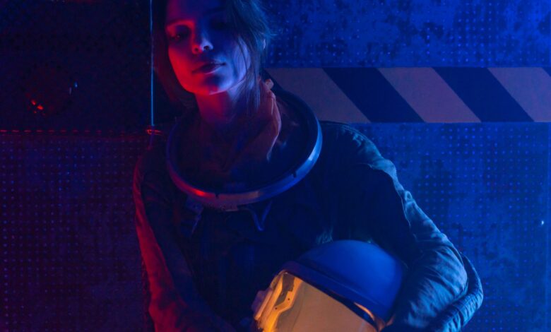 A woman astronaut in a spacesuit under vibrant red and blue lighting, evoking a futuristic, sci-fi atmosphere.