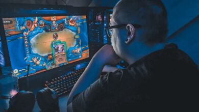 High angle of plump male gamer thinking and playing video game while sitting at table under blue light