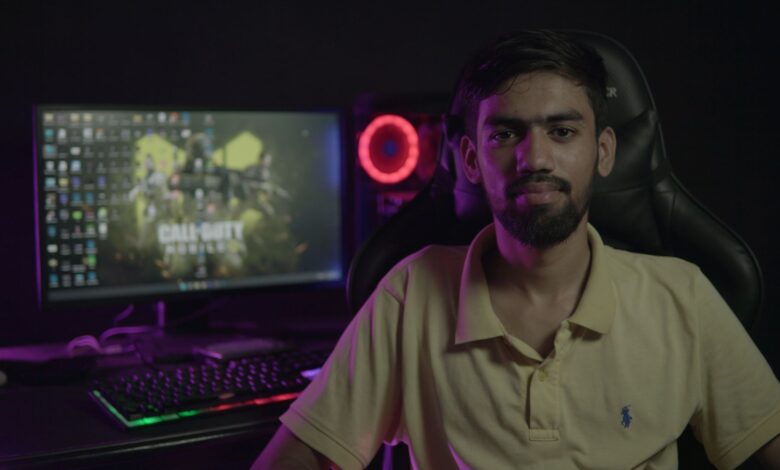 A bearded man sitting at a computer setup with a gaming PC and chair, creating a moody ambiance.