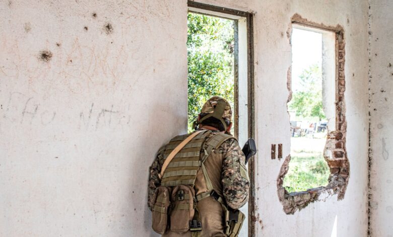 Airsoft player in camouflage navigating through a deserted, partially destroyed building.