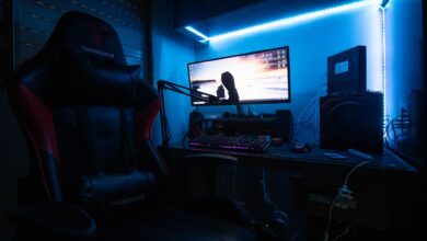 A sleek gaming desk with a monitor, gaming chair, and LED lights creating an immersive environment.
