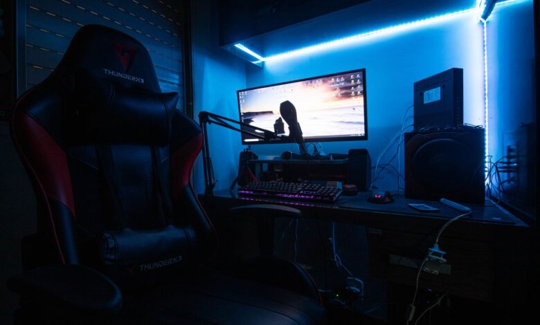 A sleek gaming desk with a monitor, gaming chair, and LED lights creating an immersive environment.