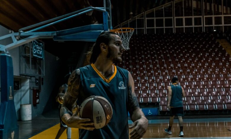 Male basketball players training and practicing in an indoor gym with basketballs and hoops.