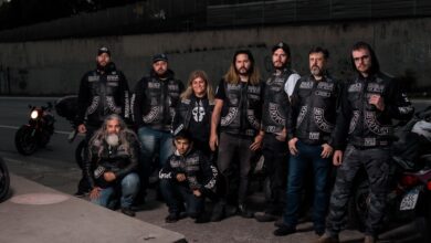 A diverse group of bikers in leather gear posing near their motorcycles on an urban street.