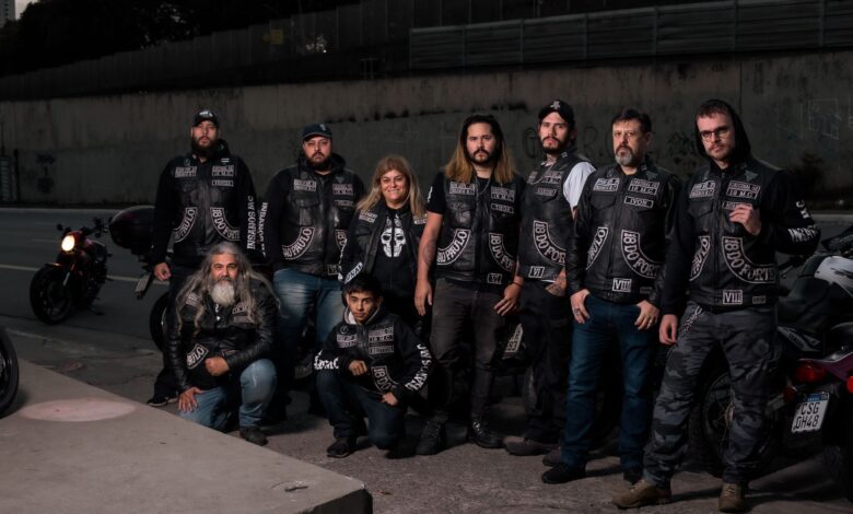 A diverse group of bikers in leather gear posing near their motorcycles on an urban street.