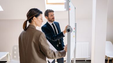 Two colleagues in formal attire discussing strategies on a whiteboard in a modern office space.