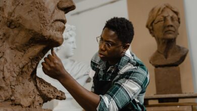 Artist meticulously shaping a clay head sculpture in an art studio, showcasing creative process.