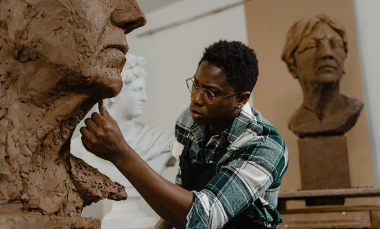 Artist meticulously shaping a clay head sculpture in an art studio, showcasing creative process.