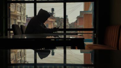Silhouette of a person in a hoodie using a smartphone inside a café with street view.