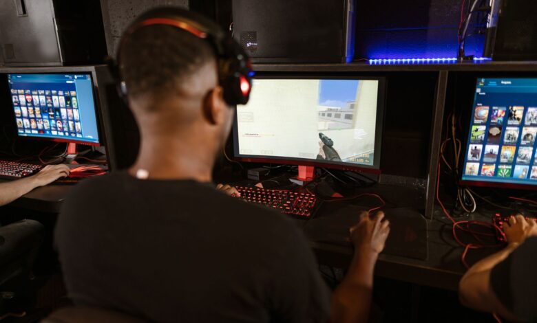 A man deeply engaged in a video game at a modern esports setup with multiple screens.