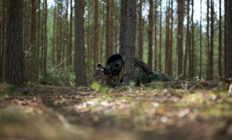 Soldier camouflaged in a forest environment, holding a weapon in a tactical stance.