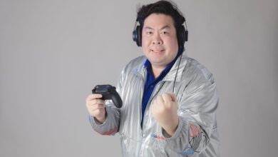 Asian man with headphones celebrates while gaming, holding a controller.