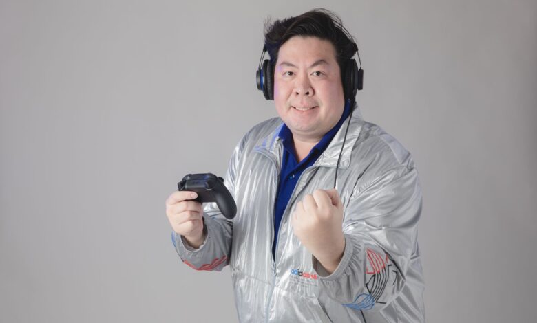 Asian man with headphones celebrates while gaming, holding a controller.