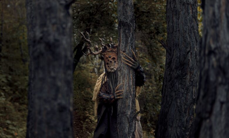 A mysterious and eerie forest scene with a costumed figure among the trees, evoking a sense of suspense.