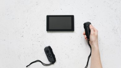 A person holds a Joy-Con controller with a Nintendo Switch on a white textured surface.