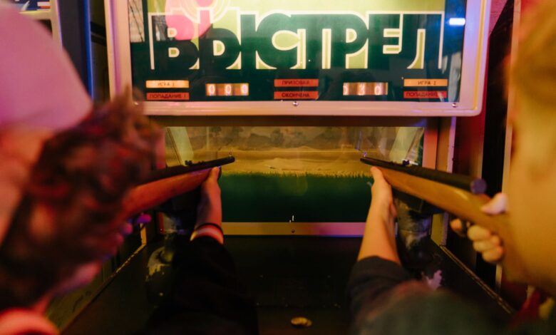Teenagers having fun playing a vintage arcade shooting game with rifles at an amusement park arcade.