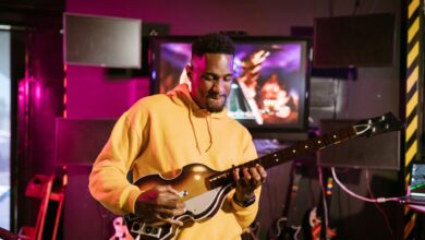 A man in a yellow hoodie plays a guitar simulation game indoors, immersed in gaming fun.