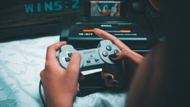 Close-up of hands holding vintage Sony controller with Sega Mega Drive in background.
