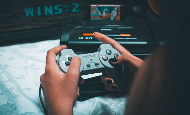 Close-up of hands holding vintage Sony controller with Sega Mega Drive in background.