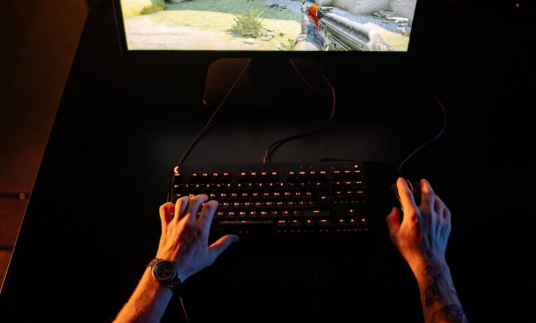 A gamer intensely playing a first-person shooter game on a computer setup indoors at night.