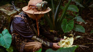 A man in steampunk attire discovers a golden artifact amidst lush green forest foliage.