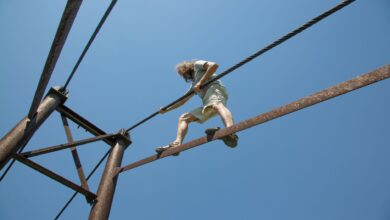 Man balances on a rope at height against clear blue sky, showcasing courage and adventure.