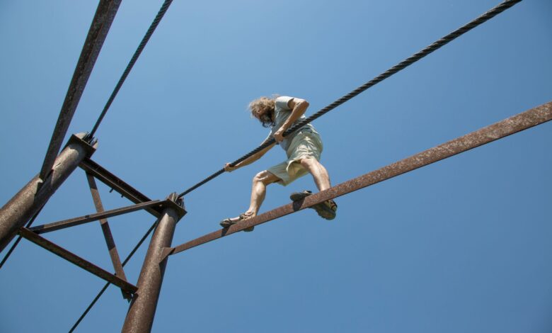 Man balances on a rope at height against clear blue sky, showcasing courage and adventure.
