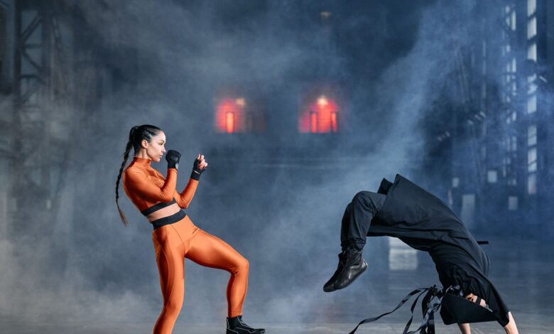 Two cosplayers in martial arts poses amidst smoke, embodying game characters in action.