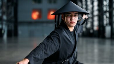 Martial artist wearing a black kimono and rice hat performing a striking pose indoors.