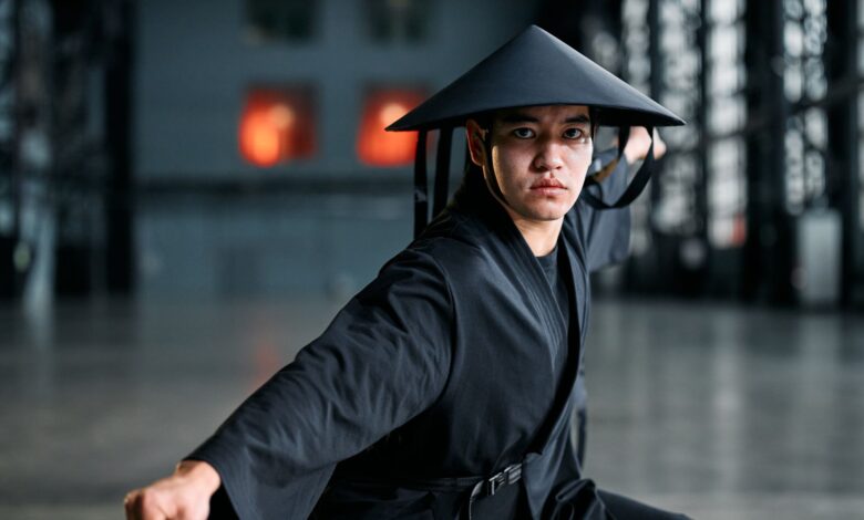 Martial artist wearing a black kimono and rice hat performing a striking pose indoors.