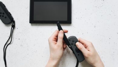 Close-up of hands holding a game controller on a white surface by a portable gaming device.