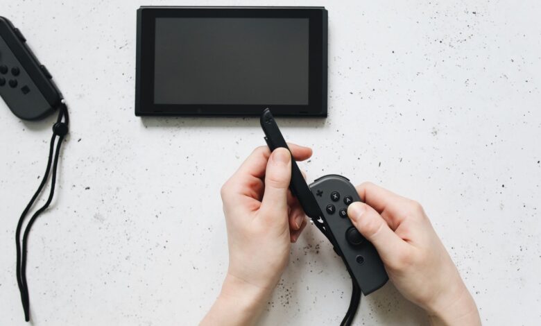Close-up of hands holding a game controller on a white surface by a portable gaming device.