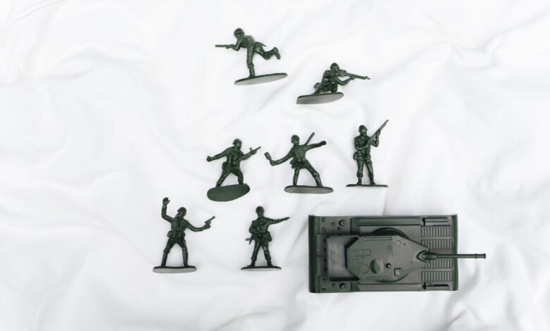 Green plastic toy soldiers and tank arranged on a white backdrop.