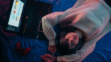 Teen girl lying on bed with laptop and game controller, perfect for gaming lifestyle visuals.