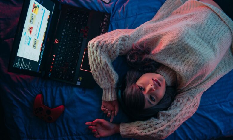 Teen girl lying on bed with laptop and game controller, perfect for gaming lifestyle visuals.