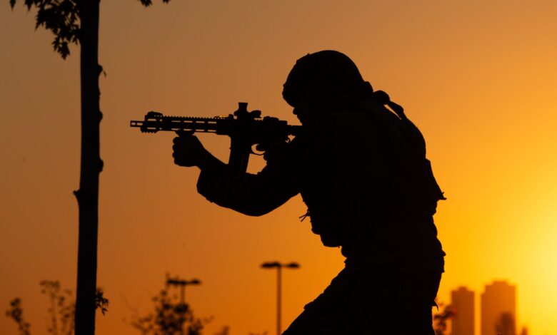 Dramatic silhouette of a soldier with a rifle against a sunrise backdrop.