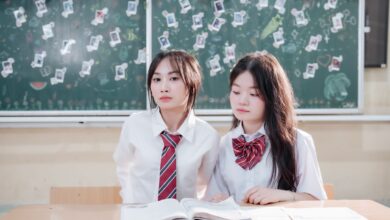 Two students in uniforms sitting at a desk with books in a classroom setting.