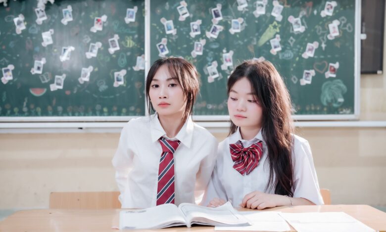 Two students in uniforms sitting at a desk with books in a classroom setting.