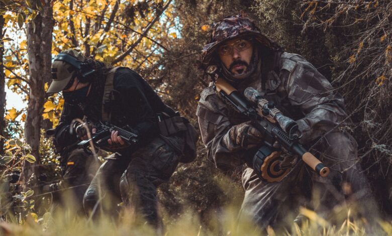 Two soldiers camouflaged in a forest, stealthily navigating with rifles in hand.