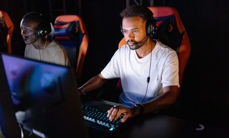Two young men engaged in an intense esports gaming session with headsets in a dark room.