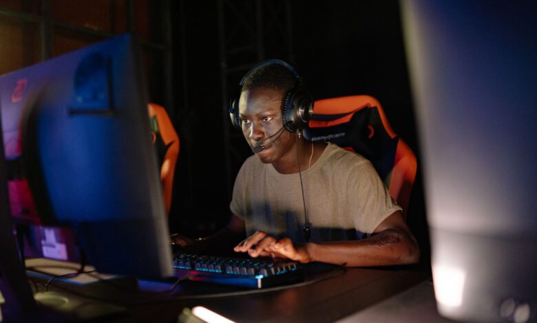 Young adult male intensely focused on computer gaming, using headset and gaming keyboard indoors.