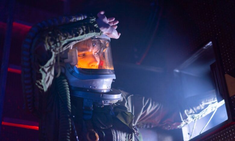 A woman in a spacesuit explores a futuristic spacecraft interior with dramatic lighting.
